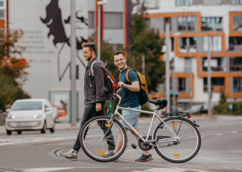 Studierende laufen mit Fahrrad über Campus